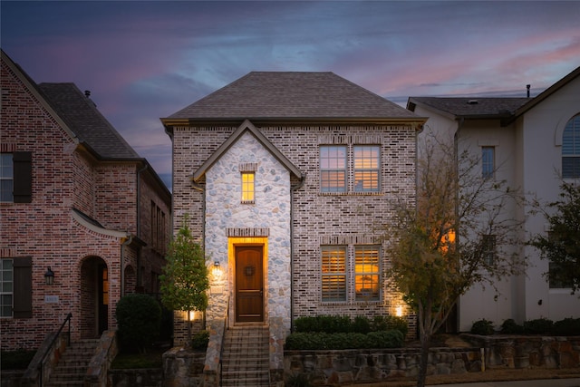 french country home featuring brick siding and roof with shingles