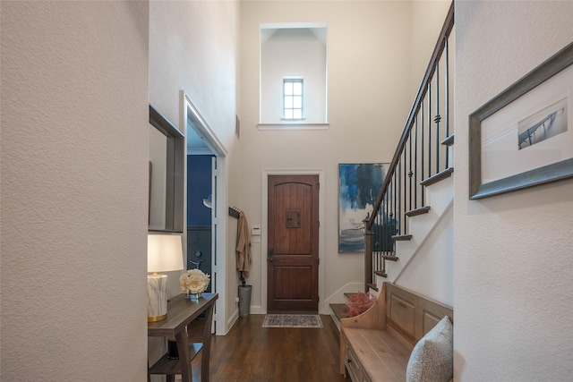 entrance foyer with dark wood-style floors, a towering ceiling, baseboards, and stairs