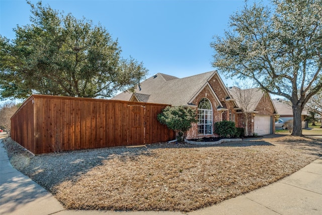 view of home's exterior featuring an attached garage, brick siding, fence, driveway, and roof with shingles