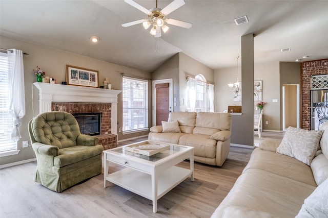 living area featuring a brick fireplace, visible vents, vaulted ceiling, and light wood-style flooring