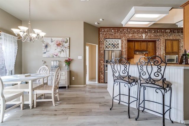 kitchen featuring brick wall, a breakfast bar area, brown cabinets, stainless steel appliances, and under cabinet range hood