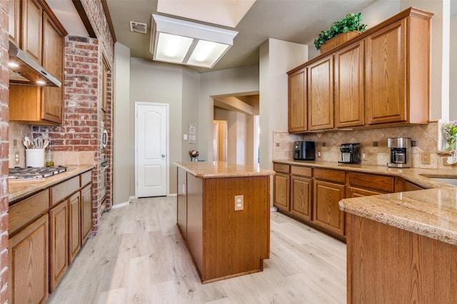 kitchen featuring a center island, stainless steel gas cooktop, tasteful backsplash, light wood-style flooring, and light stone countertops