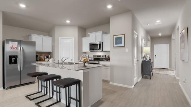 kitchen featuring stainless steel appliances, white cabinets, a sink, an island with sink, and a kitchen bar