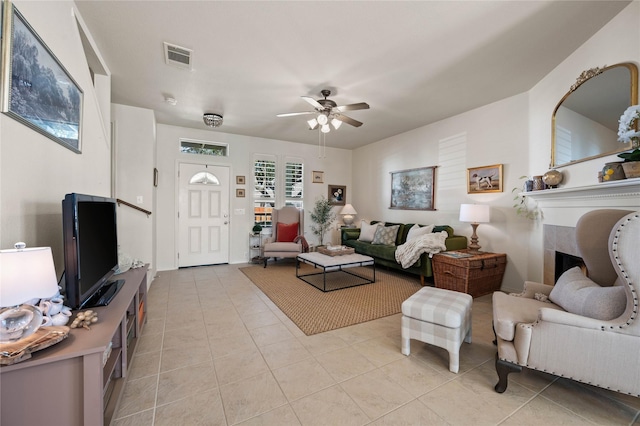 living area featuring light tile patterned floors, a fireplace, visible vents, and a ceiling fan