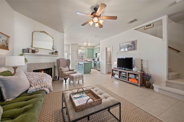 living room featuring light tile patterned floors, visible vents, a tiled fireplace, ceiling fan, and stairs