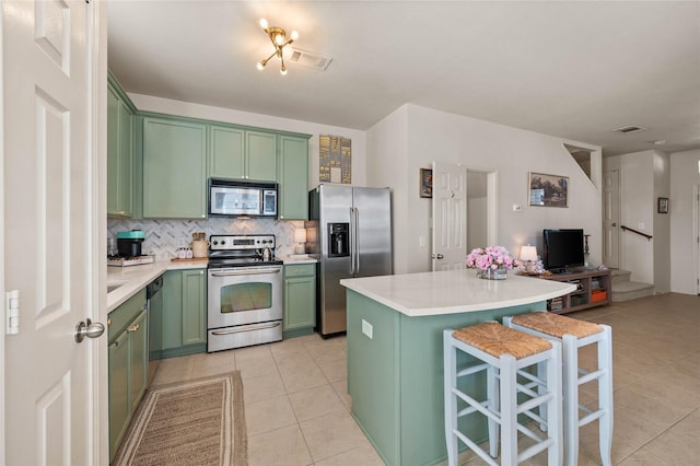 kitchen featuring decorative backsplash, stainless steel appliances, green cabinetry, and light countertops