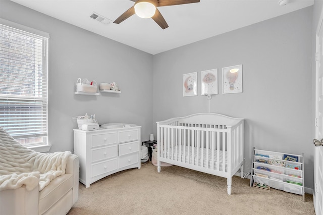 bedroom with light colored carpet, visible vents, ceiling fan, and a crib