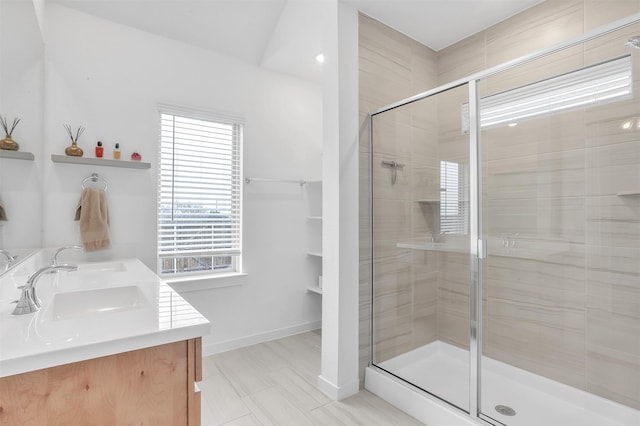 full bath with double vanity, a shower stall, baseboards, and a sink