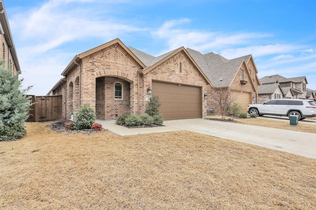 french country style house with a garage, fence, concrete driveway, and brick siding