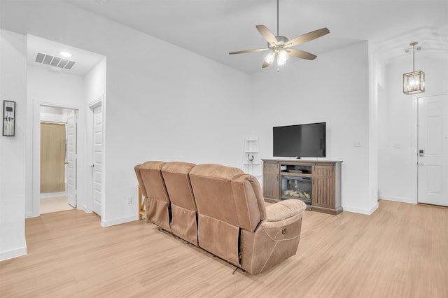 living area featuring light wood-style floors, baseboards, visible vents, and ceiling fan with notable chandelier