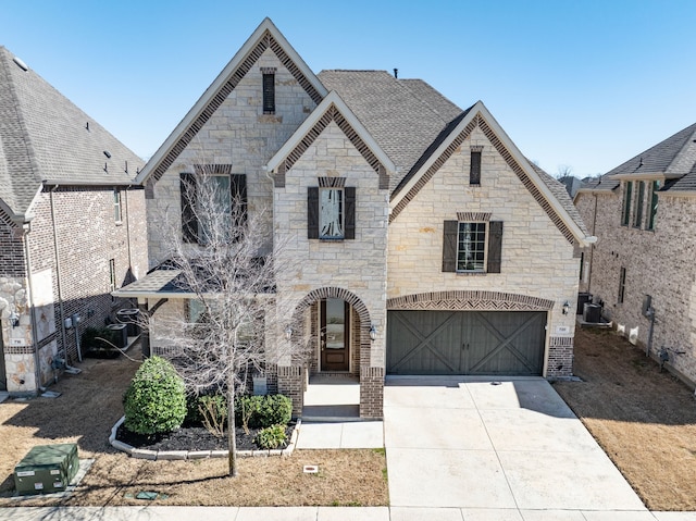 french country style house featuring roof with shingles, brick siding, concrete driveway, an attached garage, and central AC