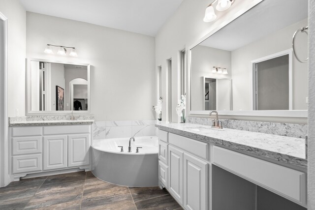 bathroom featuring a garden tub, two vanities, a sink, and wood tiled floor