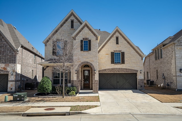 french country home featuring a garage, cooling unit, concrete driveway, and brick siding