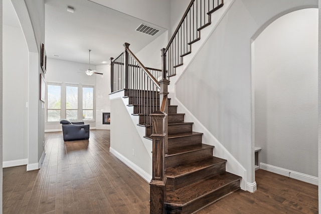 stairs with a ceiling fan, visible vents, baseboards, hardwood / wood-style floors, and a glass covered fireplace