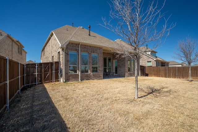 back of house featuring a shingled roof, brick siding, a lawn, and a fenced backyard