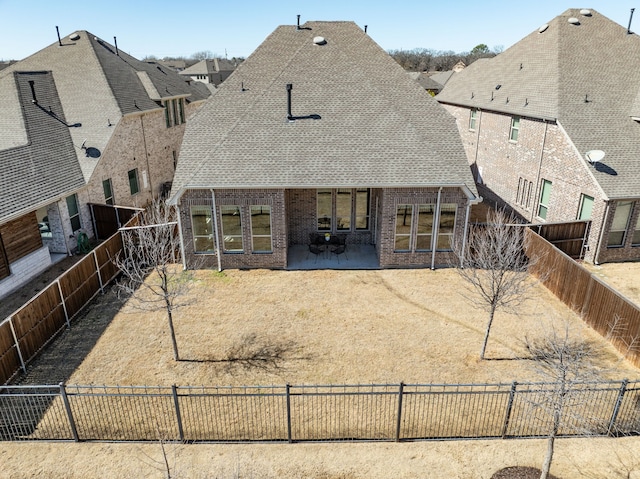 rear view of house featuring a patio, brick siding, roof with shingles, and a fenced backyard