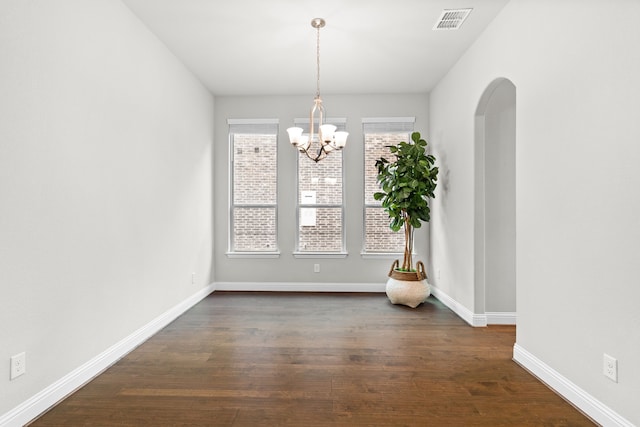 unfurnished dining area with arched walkways, visible vents, baseboards, dark wood finished floors, and an inviting chandelier