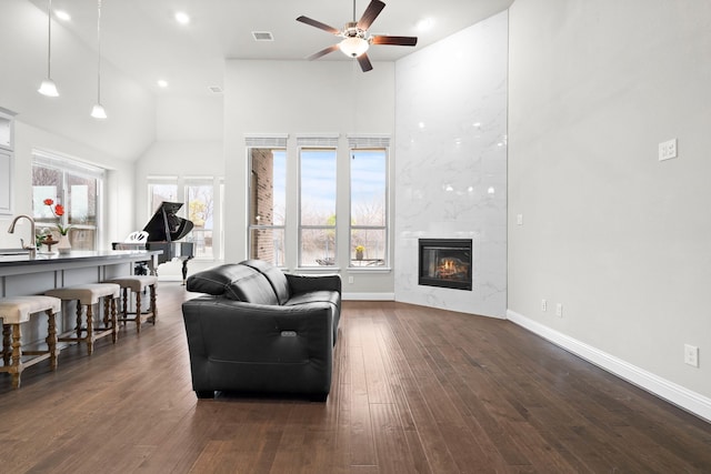 living area with dark wood-style floors, a high ceiling, a wealth of natural light, and a high end fireplace