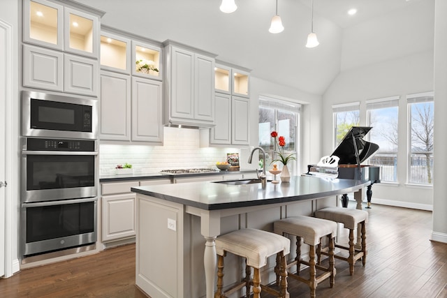 kitchen featuring dark wood-style floors, a breakfast bar area, vaulted ceiling, stainless steel appliances, and a sink