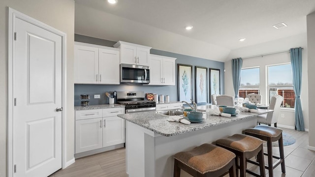 kitchen featuring a center island with sink, stainless steel appliances, visible vents, a sink, and a kitchen breakfast bar