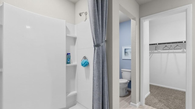 bathroom with a spacious closet, walk in shower, toilet, and baseboards