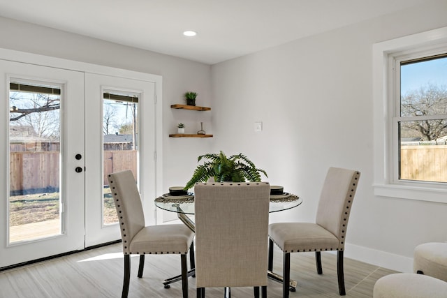 dining room featuring light wood-type flooring, french doors, a healthy amount of sunlight, and baseboards