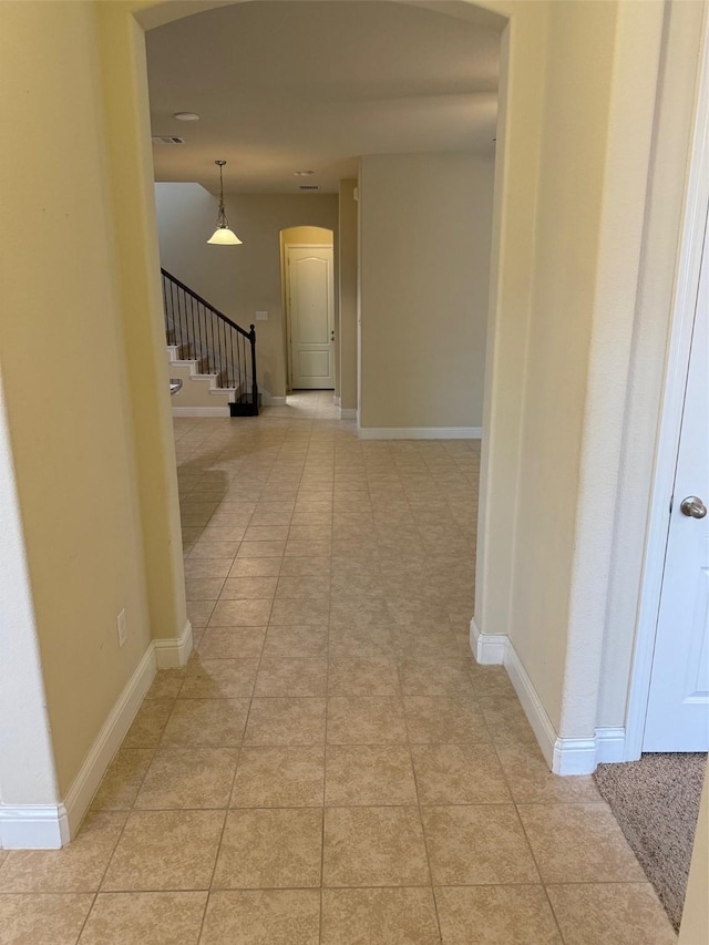 hallway featuring light tile patterned flooring, arched walkways, stairs, and baseboards