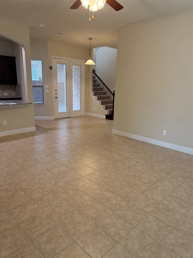 unfurnished living room featuring stairway, baseboards, visible vents, and a ceiling fan