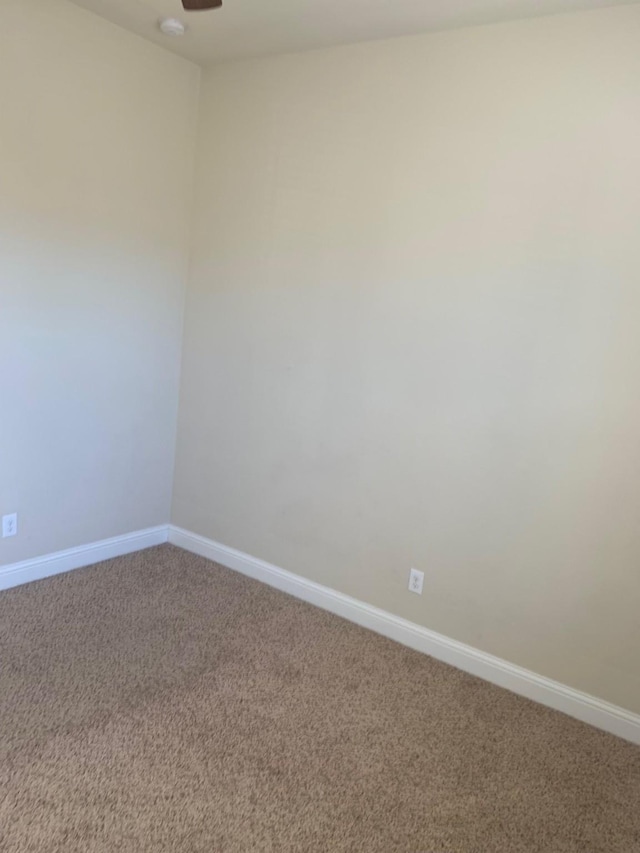 carpeted spare room with a ceiling fan and baseboards