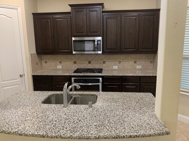 kitchen featuring a sink, decorative backsplash, light stone counters, and appliances with stainless steel finishes