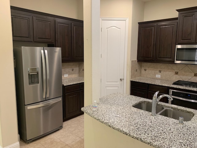 kitchen with light stone counters, light tile patterned floors, a sink, dark brown cabinets, and appliances with stainless steel finishes