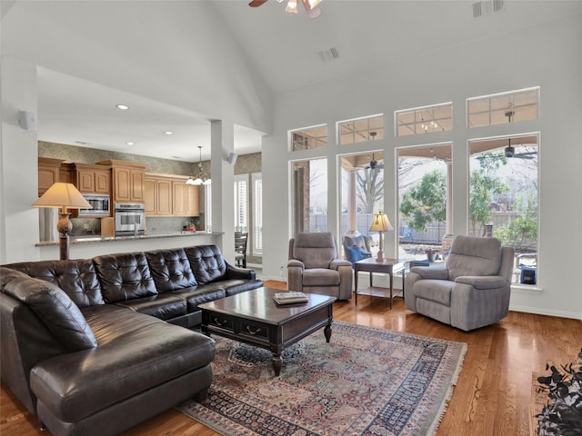 living room featuring visible vents, ceiling fan with notable chandelier, high vaulted ceiling, and wood finished floors