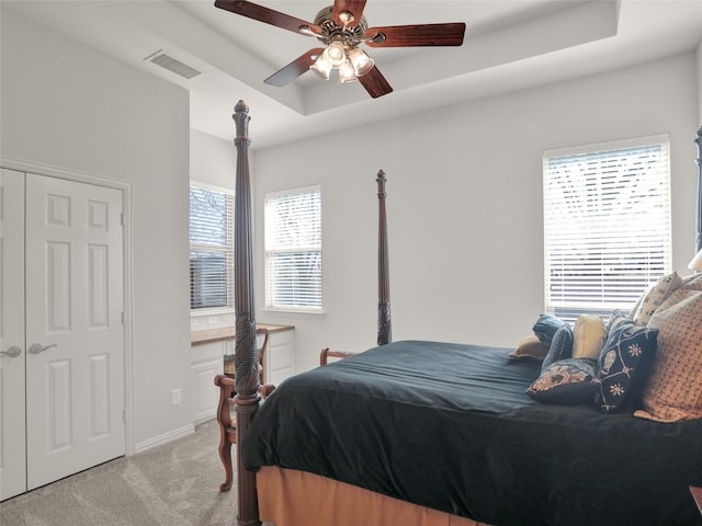 bedroom with a ceiling fan, visible vents, baseboards, a raised ceiling, and light colored carpet