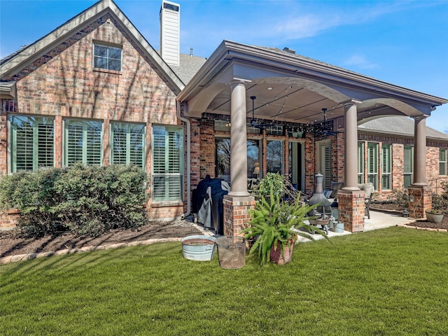 rear view of house featuring brick siding, a patio area, a lawn, and a chimney