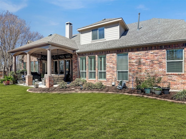 back of property featuring a patio, a yard, a chimney, a shingled roof, and brick siding