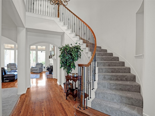 staircase featuring arched walkways, baseboards, a towering ceiling, and wood finished floors