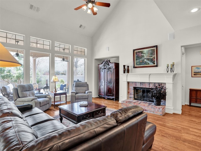 living area featuring visible vents, a fireplace, light wood-type flooring, and ceiling fan