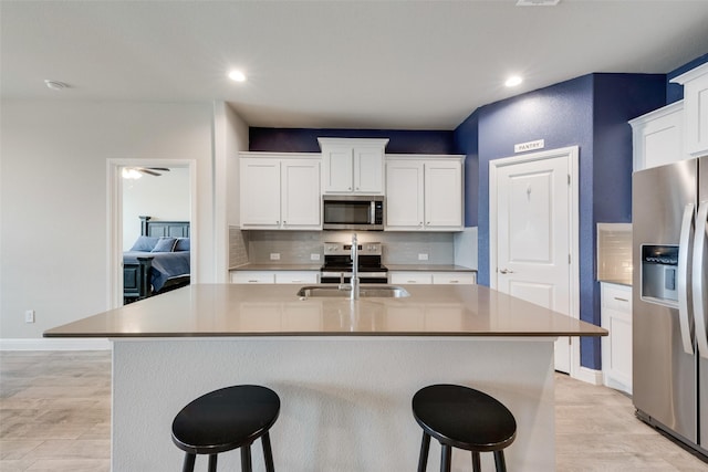 kitchen featuring stainless steel appliances, a breakfast bar area, backsplash, and white cabinetry