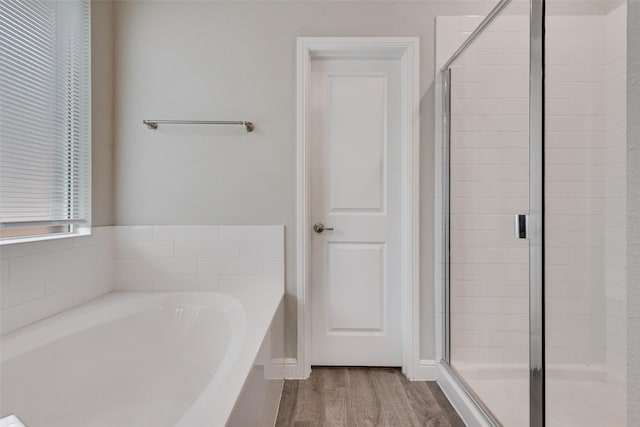 bathroom with a stall shower, a bath, and wood finished floors