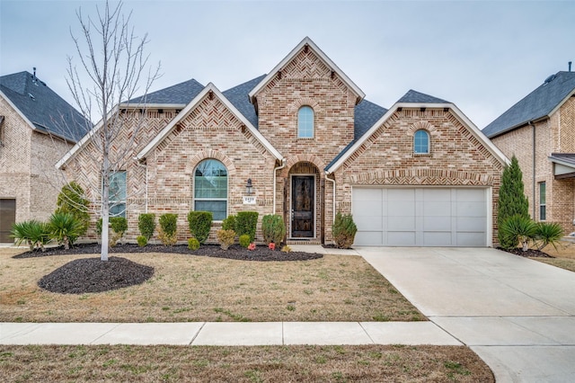 french country inspired facade with a garage, brick siding, driveway, roof with shingles, and a front yard