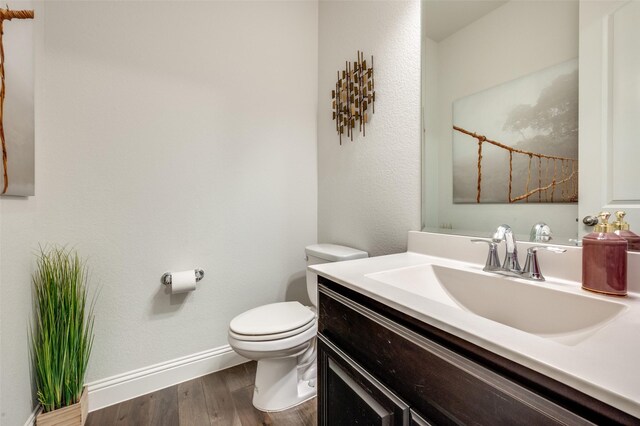 half bathroom with toilet, baseboards, wood finished floors, and vanity