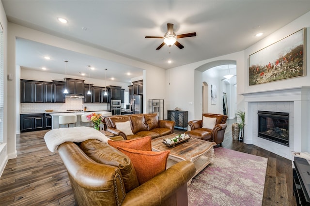 living area with arched walkways, a tile fireplace, ceiling fan, dark wood-type flooring, and recessed lighting