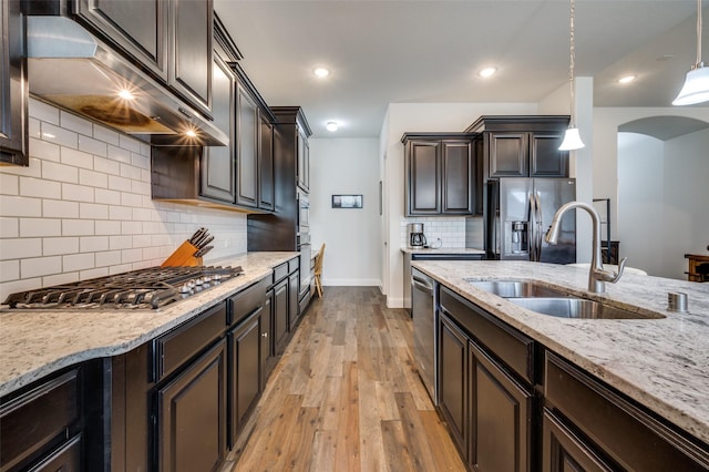 kitchen featuring stainless steel appliances, exhaust hood, a sink, light wood-type flooring, and light stone countertops