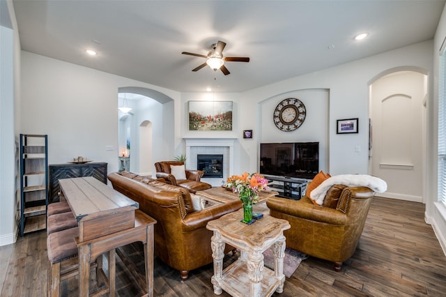 living room with a ceiling fan, arched walkways, dark wood-style flooring, and a fireplace