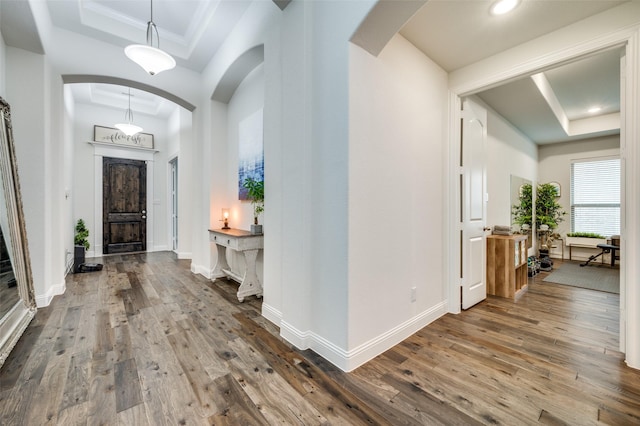 foyer featuring arched walkways, a raised ceiling, hardwood / wood-style flooring, and baseboards