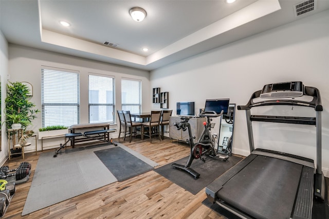 workout area featuring a tray ceiling, visible vents, and wood finished floors