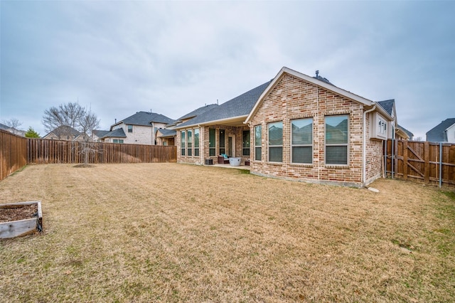 back of property featuring a fenced backyard, a lawn, and brick siding