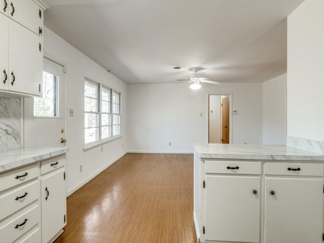 kitchen featuring baseboards, a peninsula, light countertops, light wood-type flooring, and white cabinetry