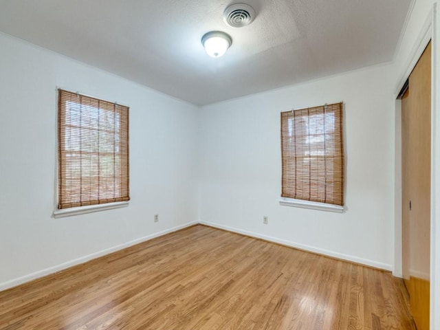 empty room with light wood-style floors, baseboards, and visible vents