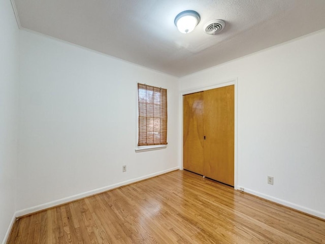 spare room featuring light wood-type flooring, baseboards, visible vents, and ornamental molding